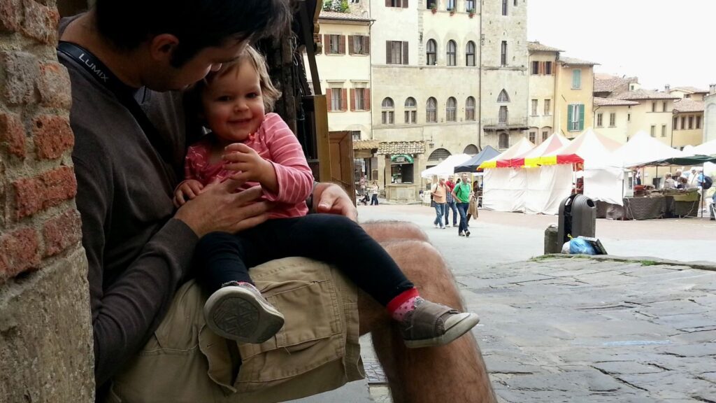 baby and father sitting in a doorway eating a snack on a street in Tuscany, Italy