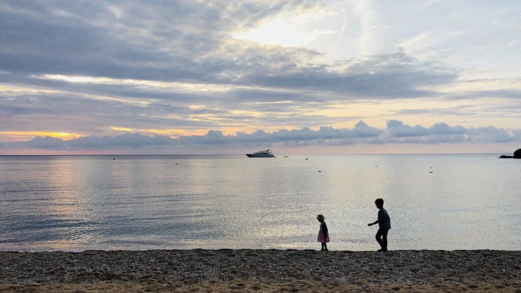 a toddler and a child walking on beach at sunset