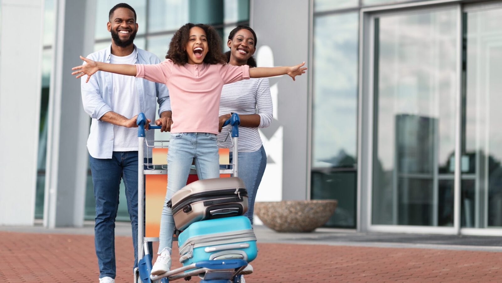 Happy kid standing on luggage cart as family leaves airport on a stopover