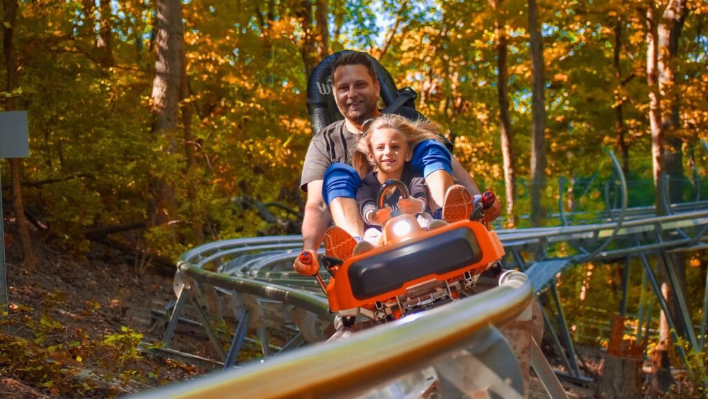 A father and child riding the Aerie's mountain coaster during the fall in the Great Rivers & Routes region of Illinois