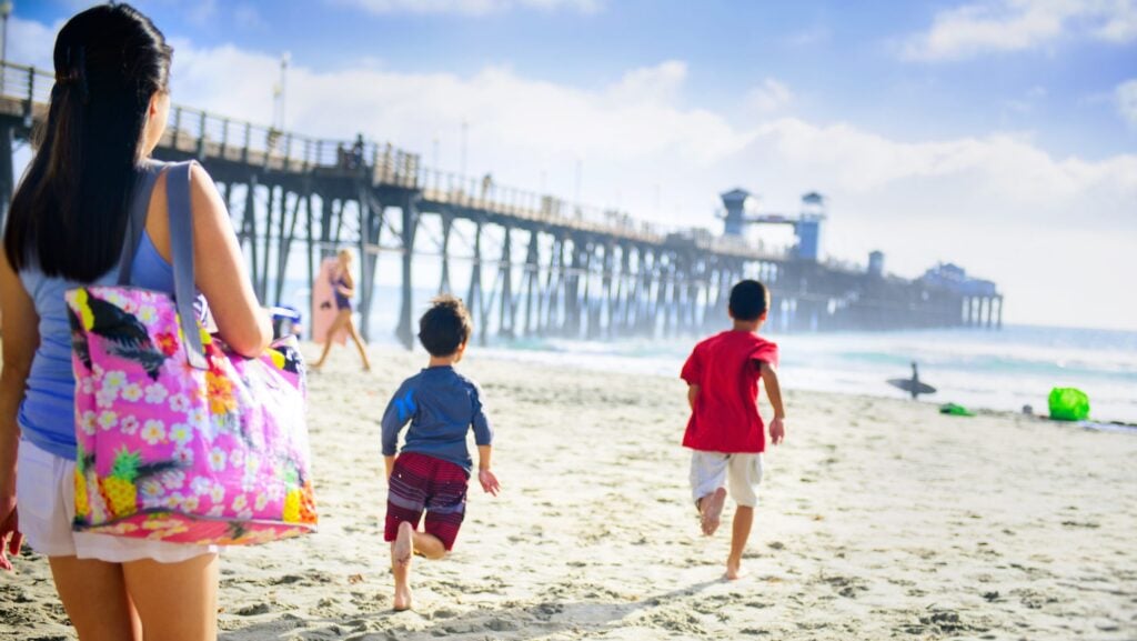 children running toward the ocean at the beach in Oceanside, California near the pier