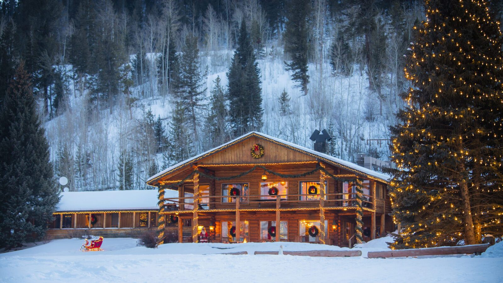 A cabin and tree decorated for the holidays in the snow