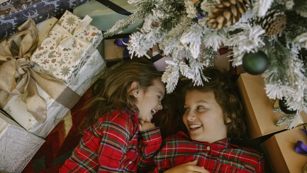 Two girls in plaid pajamas lying under a Christmas tree