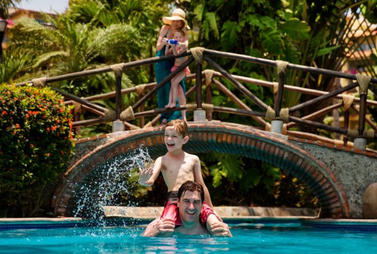 A mom and daughter squirting a squirt gun from a bridge at a dad and son in the pool