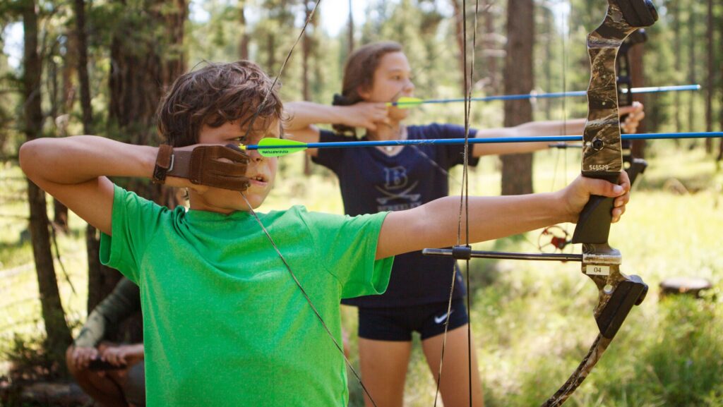 Two kids doing archery in the woods at Paws Up Montana