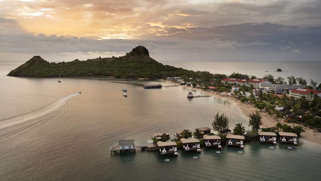 A sunset aerial view of the beach, overwater bungalows, and resort buildings at Sandals Grande Saint Lucian