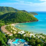 An aerial view of Carlisle Bay resort with water, the beach, boats, and green hills