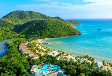 An aerial view of Carlisle Bay resort with water, the beach, boats, and green hills
