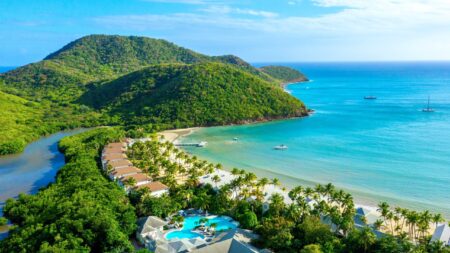 An aerial view of Carlisle Bay resort with water, the beach, boats, and green hills