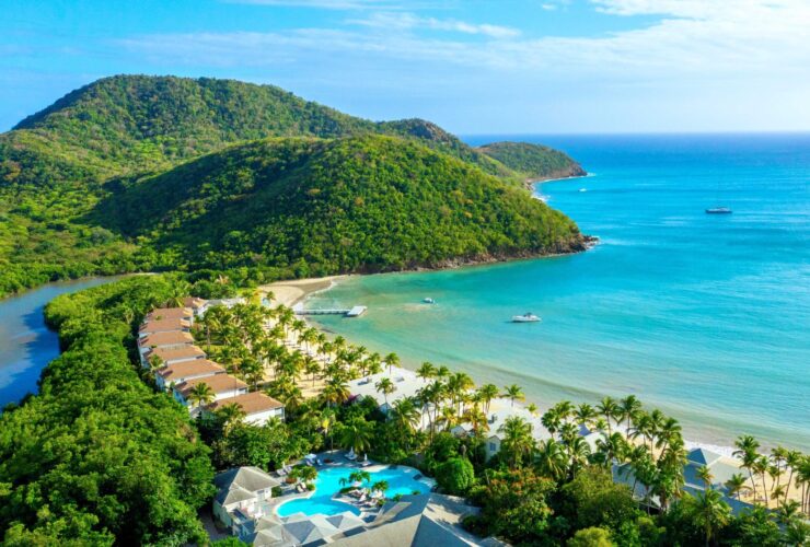An aerial view of Carlisle Bay resort with water, the beach, boats, and green hills