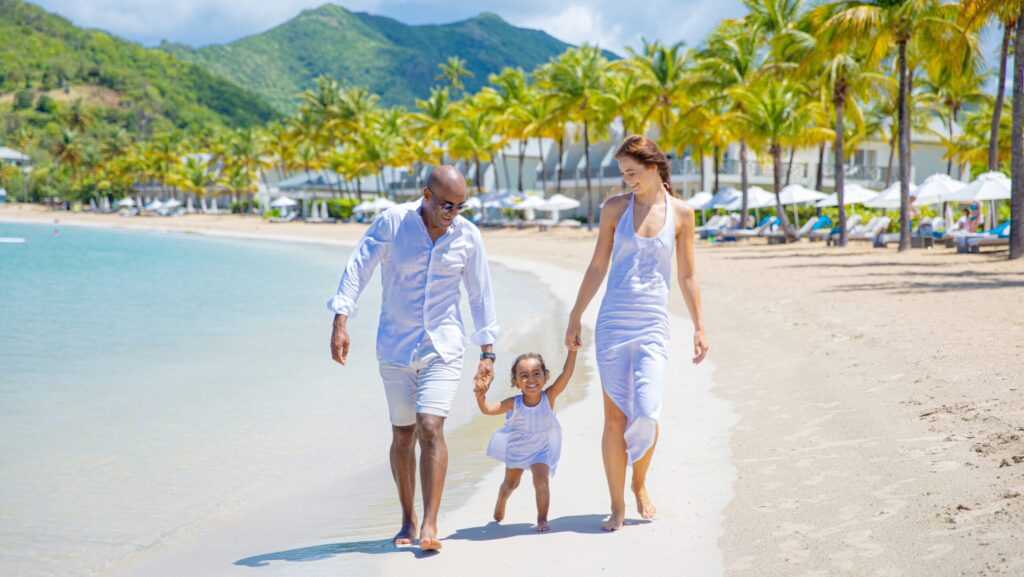 Parents and a small child holding hands and walking on the beach with mountains in the distance at Carlisle Bay
