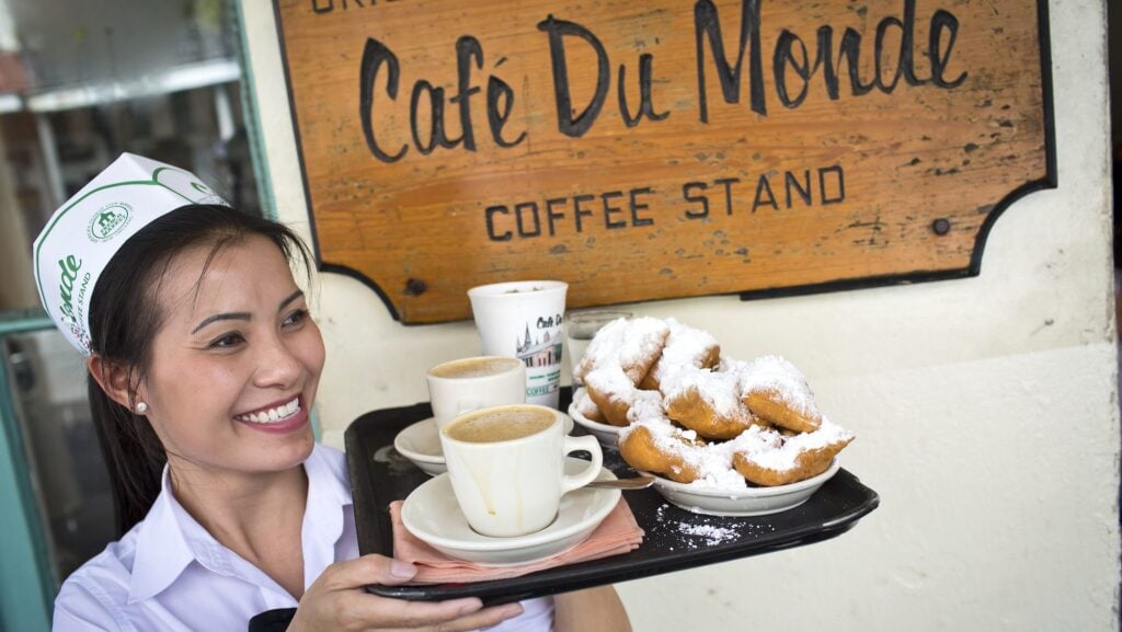 server at Cafe du Monde holding tray of coffee and beignets