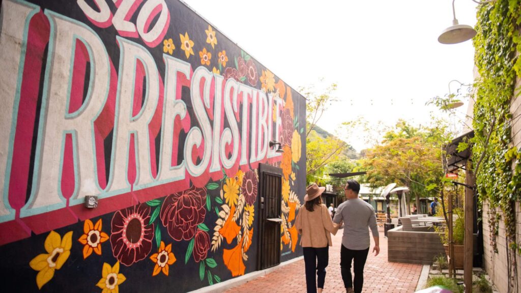 couple wandering past mural that says SLO Irresistible in San Luis Obispo, California