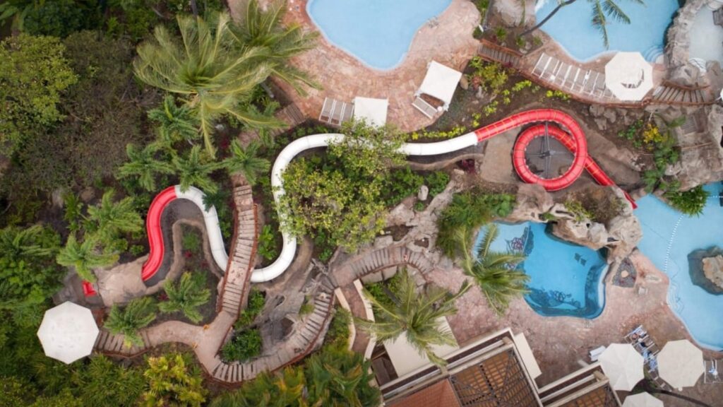 An aerial view of a red and white waterslide and several pools at Grand Wailea 