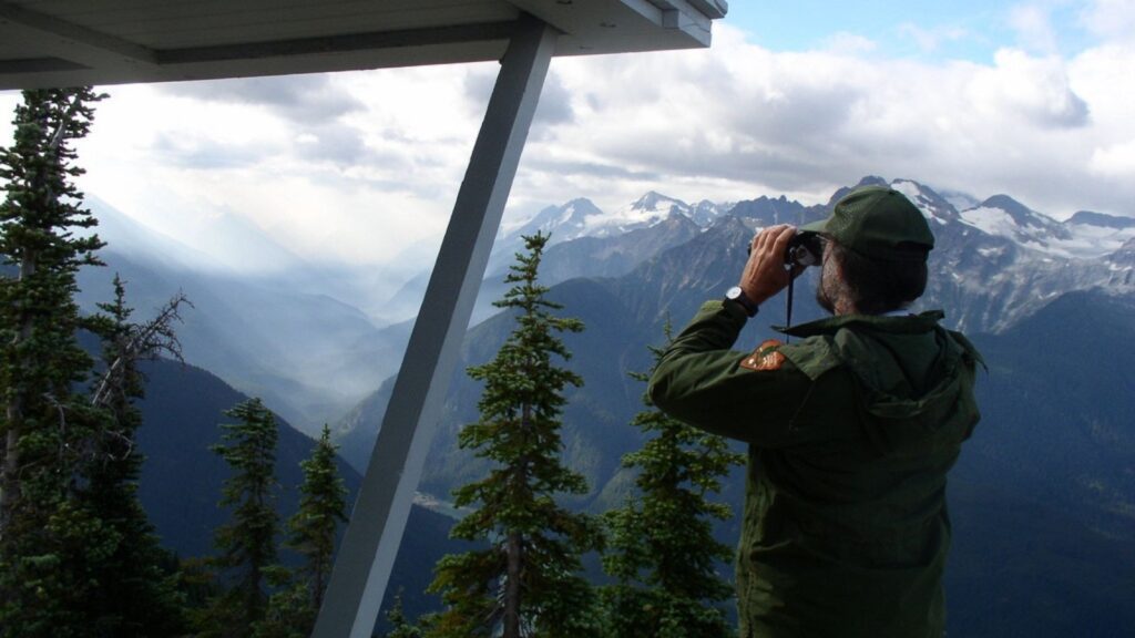 Ranger looking out at the North Cascades terrain from the Sourdough Fire Lookout in North Cascades National Park