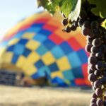 close up of grapes in Napa with a hot air balloon being slowly inflated in the background