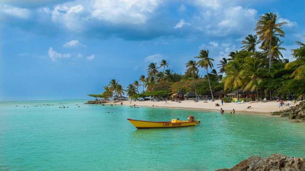 Beach on Tobago island with boat in water and people swimming