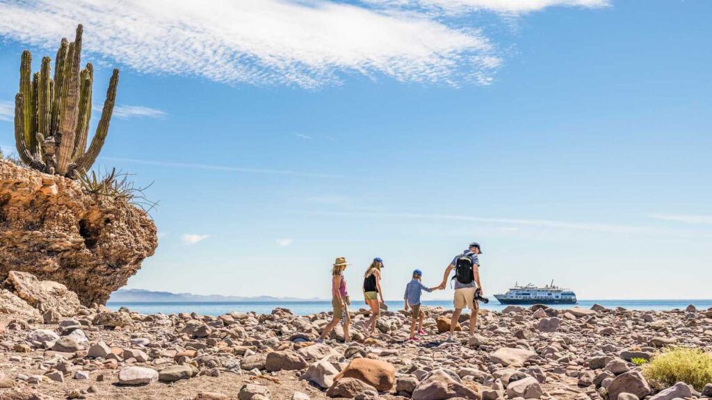 Family walking on rocky beach with small expedition cruise ship in the background