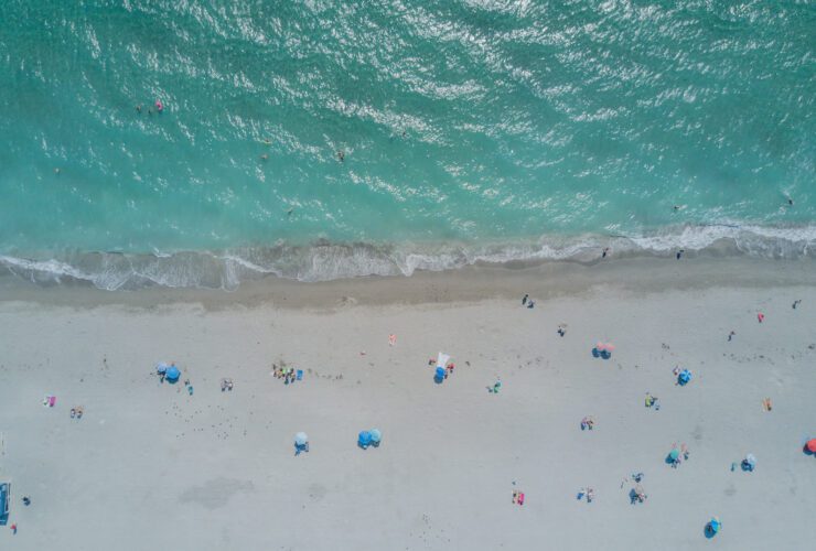 Aerial view of beach with clear turquoise water and white sand dotted with beach umbrellas, people, and chairs