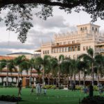 Palatial-style resort building at sunset with a large green lawn space in the forefront adorned by string lights and with families playing games