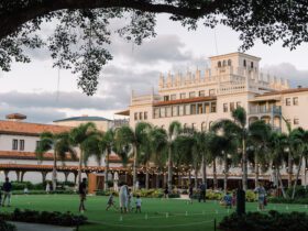 Palatial-style resort building at sunset with a large green lawn space in the forefront adorned by string lights and with families playing games