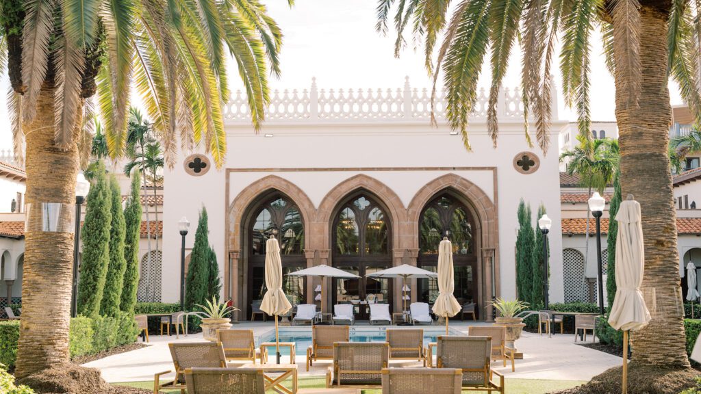 Palatial-style building with large arched windows set behind pool and flanked by two palm trees