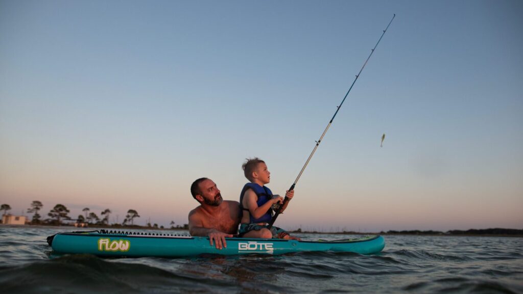 A man and child fishing from a paddleboard at sunset