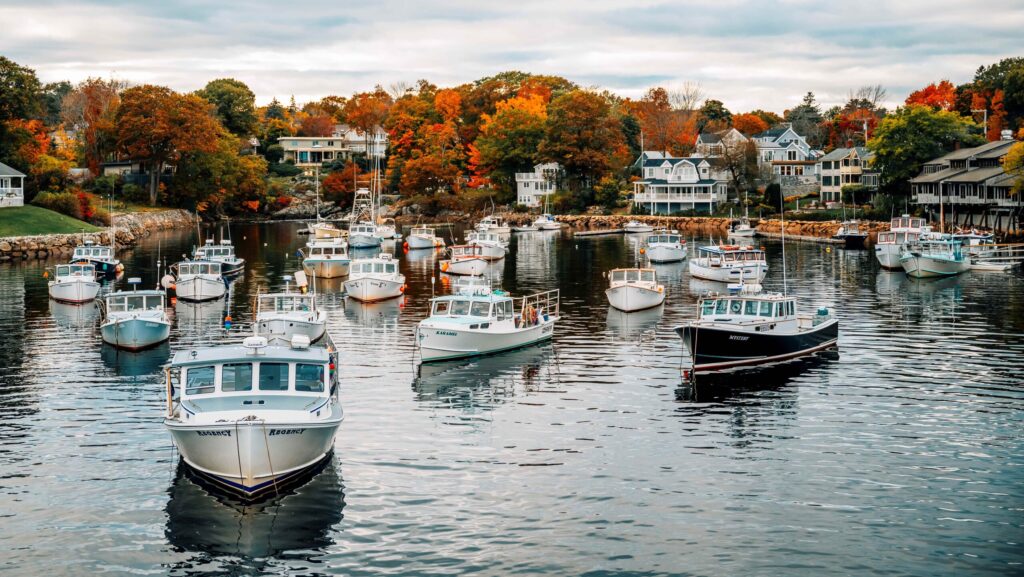 Boats in the water with fall foliage behind them in Ogunquit, Maine