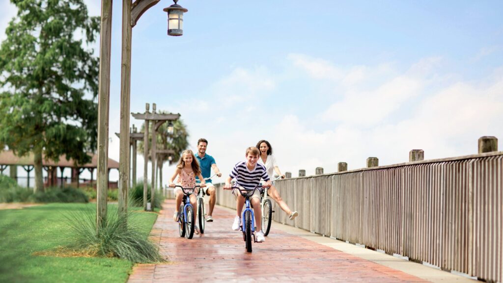 A family riding bikes on a brick pathway by the water at Grand Hotel Golf Resort & Spa 