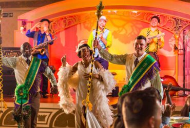 Actors dressed in New Orleans-style costumes singing and dancing on a colorful stage