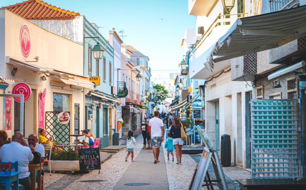 Family with two young children walking down a crowded, cobblestone street running through whitewashed buildings