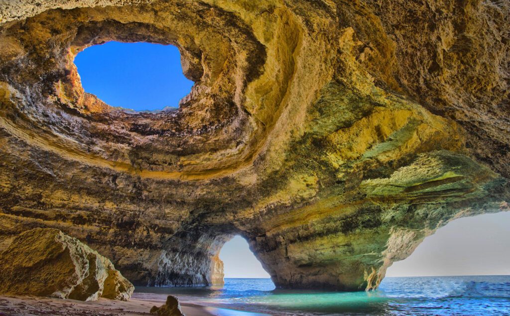 View looking up from inside a seaside cave, with a hole on the ceiling peeking through to the sky