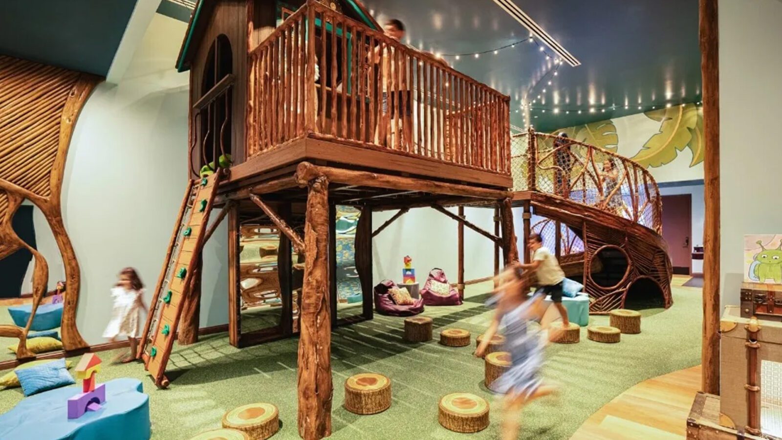 Kids running around a treehouse play structure inside a building