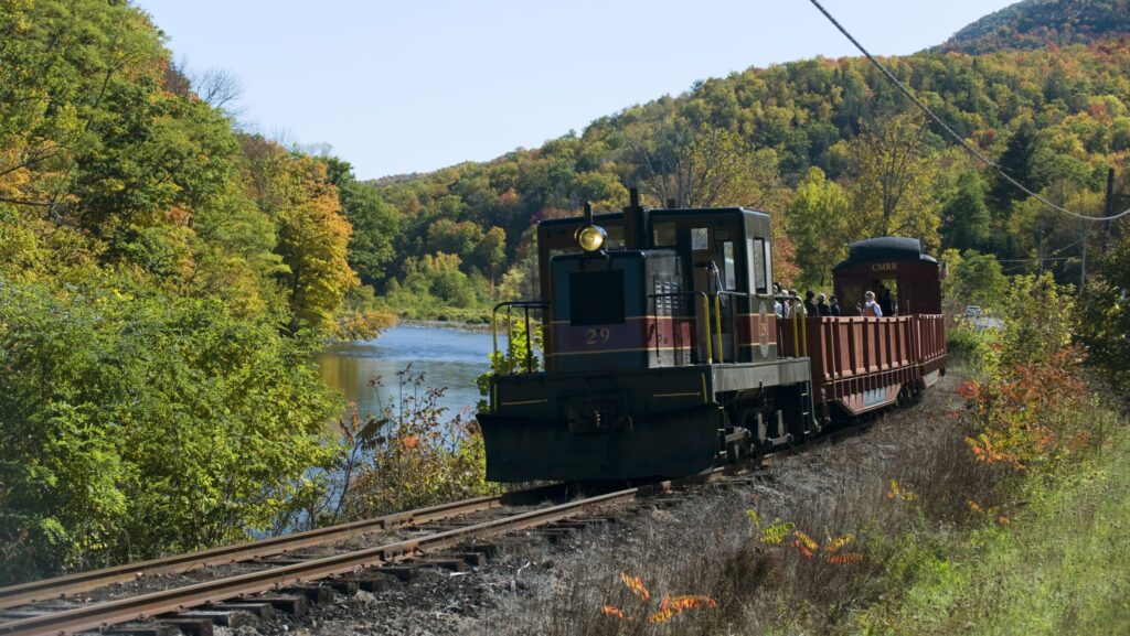 A Catskill Mountain Railroad train riding on the tracks through fall foliage