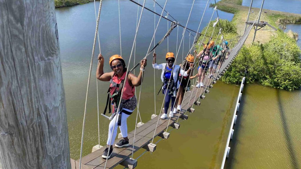 A family wearing safety harnesses crosses a suspension bridge over wetlands