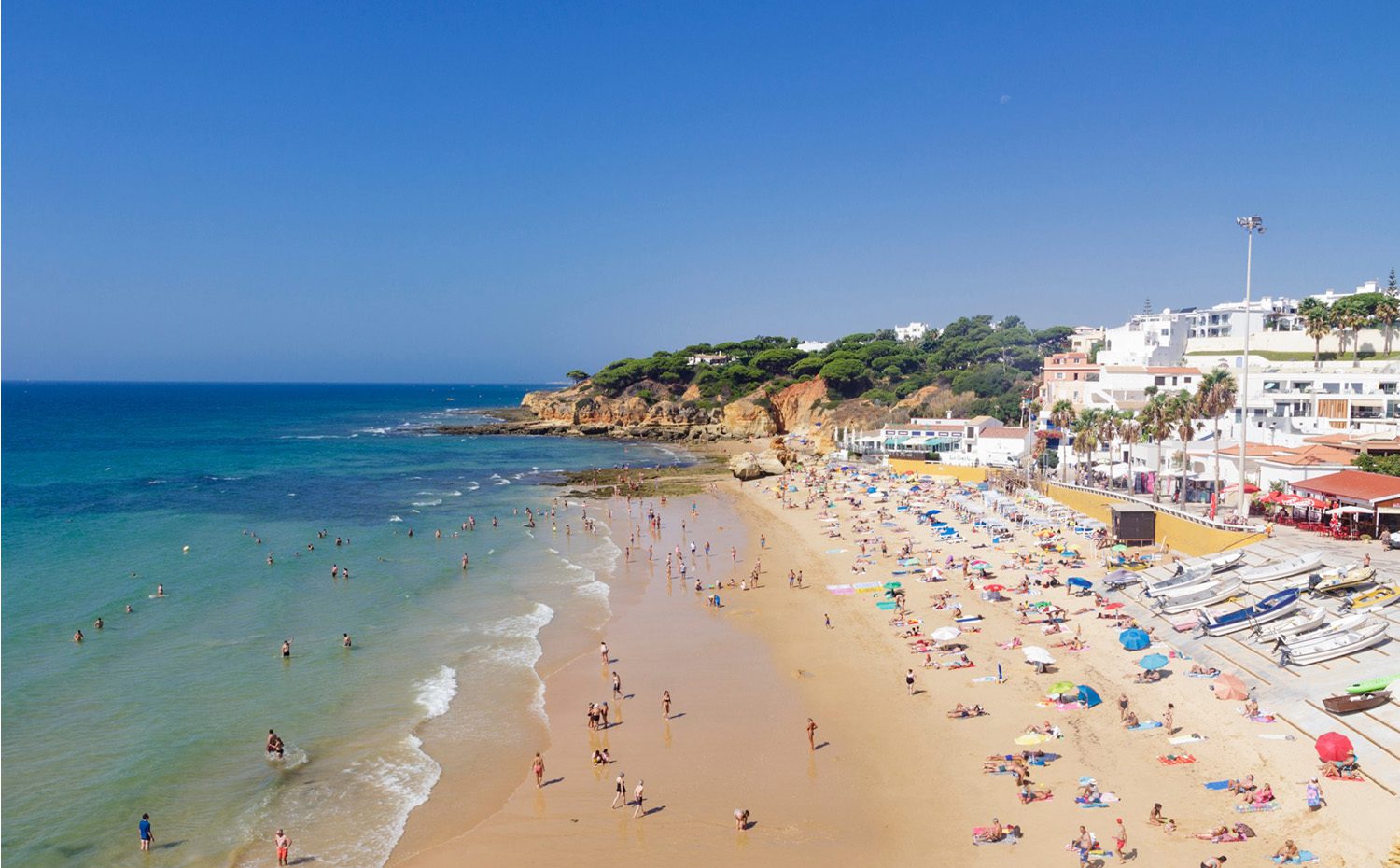 Golden san beach with turquoise water, with rocky bluff and whitewashed buildings in the background