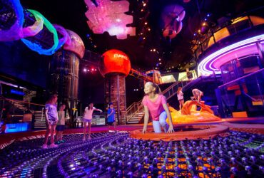 Kids play in dark, colorful space with planet structures hanging from the ceiling