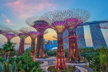 Futuristic buildings and colorful structures in a tree-lined park at sunset