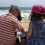 two children sitting on a beach digging in the sand with a bucket