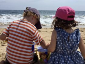 two children sitting on a beach digging in the sand with a bucket