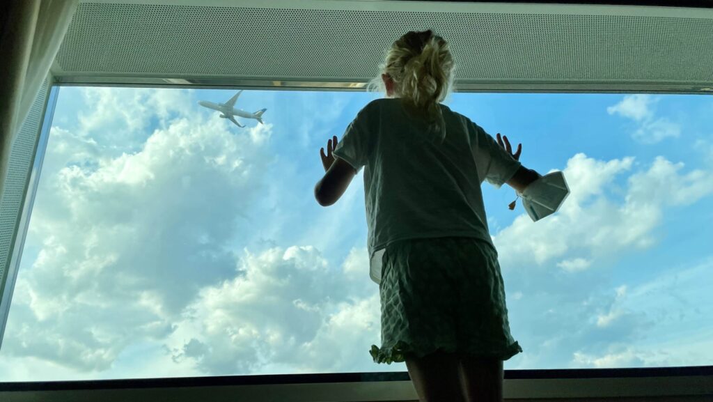 child looking out airport hotel window in London watching a plane take off