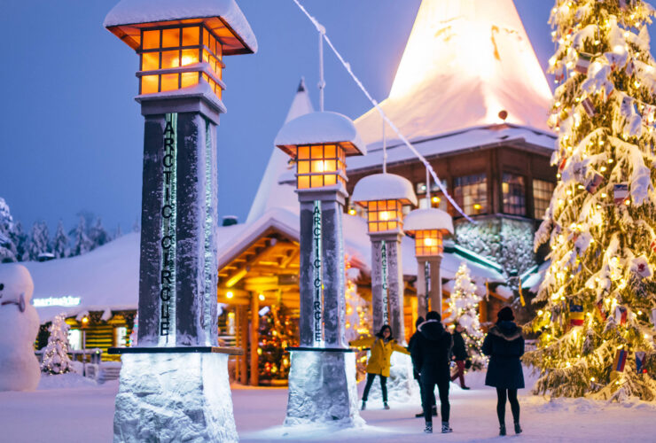 A snowy village surrounded by lanterns, a tall Christmas tree, and people walking around