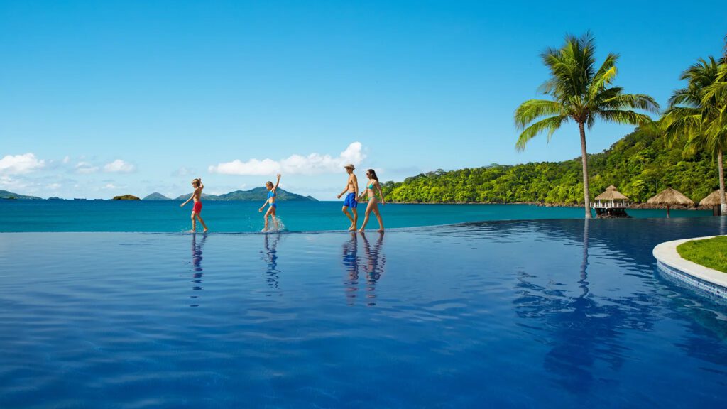 A mother, father, young son, and daughter walking along an infinity-edge pool with the ocean and mountains in the background