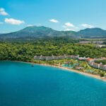 White resort with a terracotta roof surrounded by dense rainforest with mountains in the background and the beach in the foreground