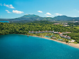 White resort with a terracotta roof surrounded by dense rainforest with mountains in the background and the beach in the foreground