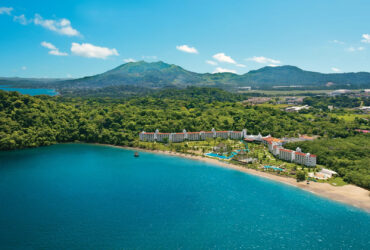 White resort with a terracotta roof surrounded by dense rainforest with mountains in the background and the beach in the foreground