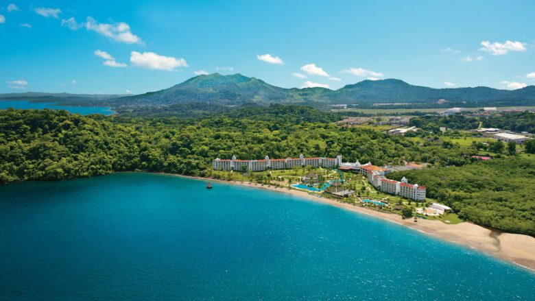 White resort with a terracotta roof surrounded by dense rainforest with mountains in the background and the beach in the foreground