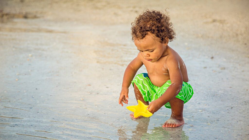 Baby boy squatting on the beach and playing with a toy star