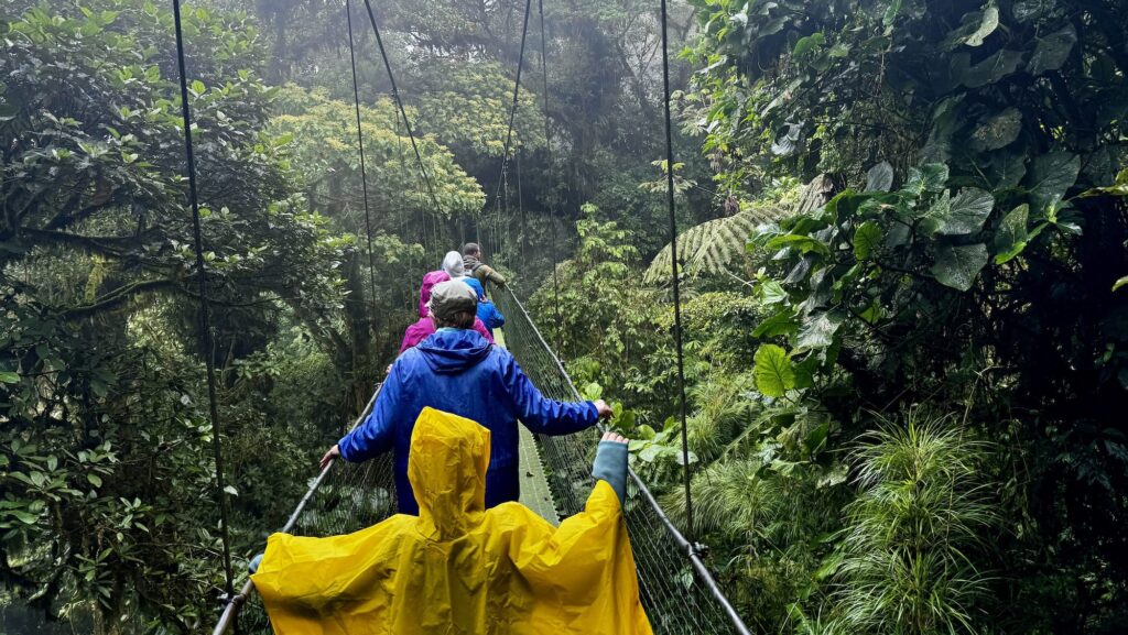 child and adults in rain gear crossing a suspension bridge in Costa Rica