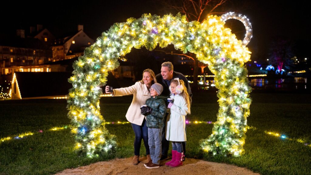 A family taking a selfie under an illuminated arch during the Winter Wander Trail of Lights at Boar's Head Resort